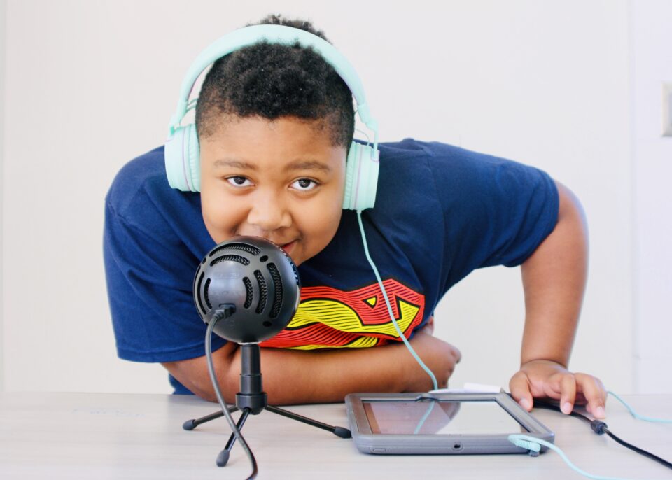 A young person wearing headphones smiling and speaking into a microphone.
